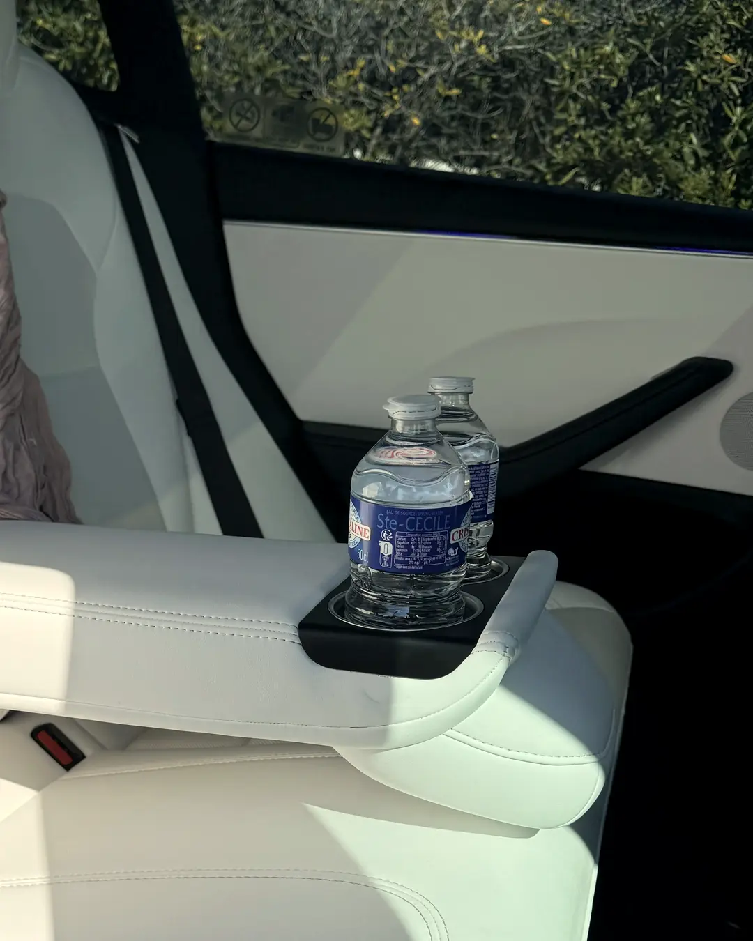Accoudoir central en cuir blanc déplié à l’arrière de la Tesla Model 3 ELYSIA, deux bouteilles d’eau fraîche dans le porte-gobelet