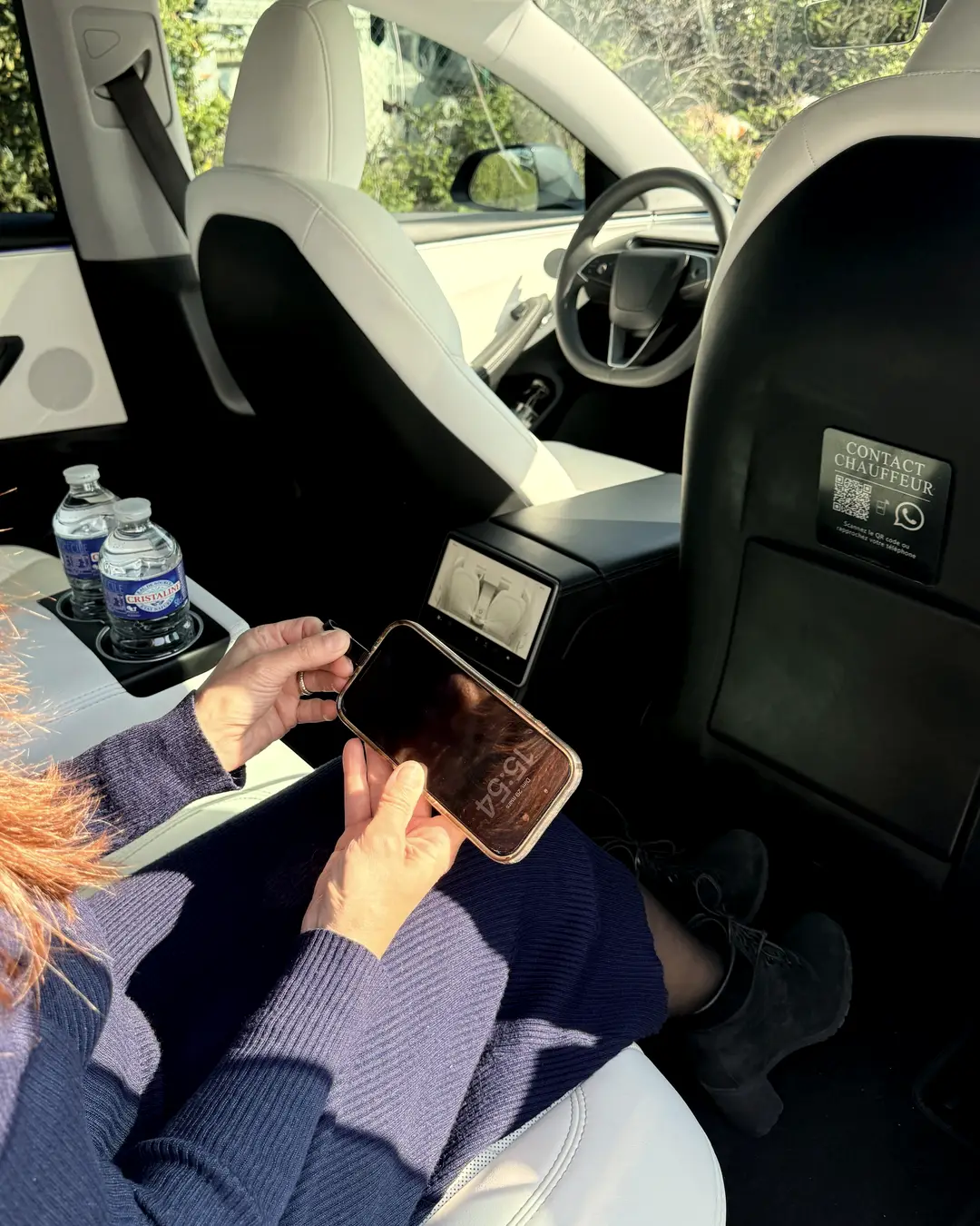 Une passagère installée à l’arrière de la Tesla Model 3 ELYSIA consulte son téléphone, eau fraîche à portée de main