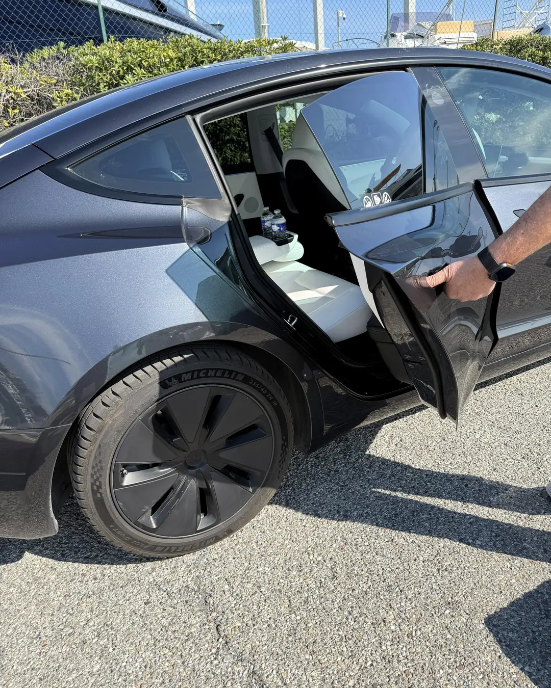 Le chauffeur ELYSIA ouvre la portière arrière de la Tesla Model 3, intérieur blanc visible, au bord d’un port