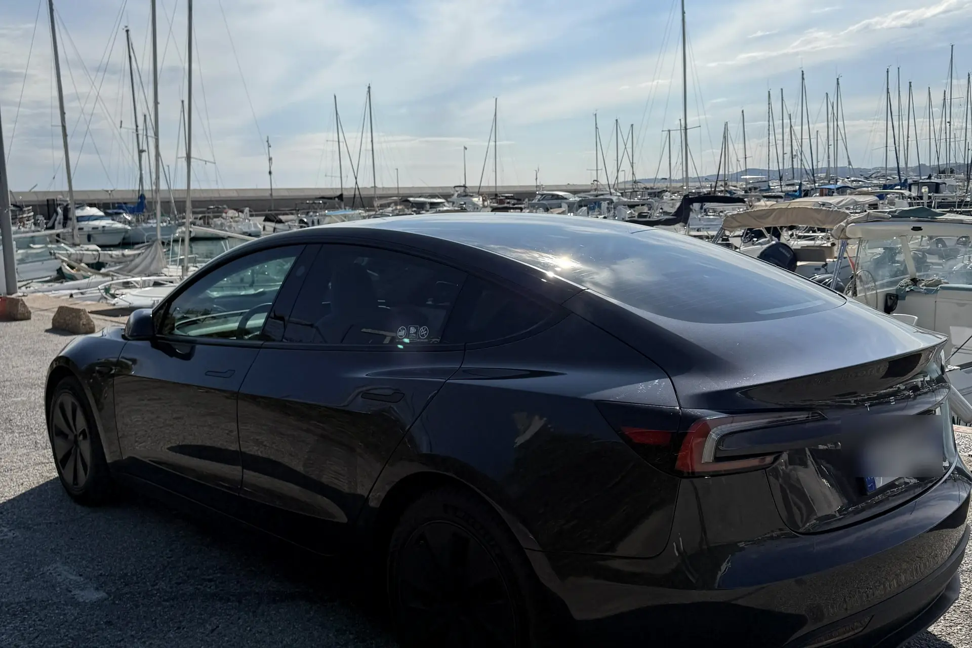 La Tesla Model 3 noire d’ELYSIA vue de trois quarts arrière, devant les mâts d’un port de la Côte d’Azur